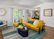Thumbnail 8 of 27 - A living room with a yellow couch and a blue coffee table.