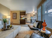 Thumbnail 5 of 16 - A living room with a black leather couch, a coffee table, and a potted plant.