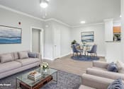 Thumbnail 4 of 23 - A living room with a grey couch, a glass coffee table, and a painting of a beach scene on the wall.