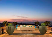 Thumbnail 18 of 21 - A patio with a couch, chairs, and a table with lights is set up on a rooftop.