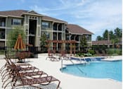 Thumbnail 15 of 19 - A pool area with chairs and a building in the background.