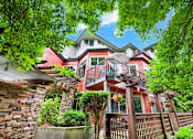 Thumbnail 22 of 23 - A house with a red and white exterior is surrounded by trees and greenery.