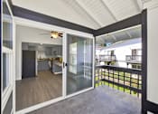 Thumbnail 26 of 33 - A balcony with a glass railing and sliding glass doors leading to a kitchen.