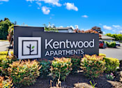 Thumbnail 10 of 21 - A sign for Kentwood Apartments is surrounded by shrubbery.
