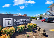 Thumbnail 12 of 21 - A sign for Kentwood Apartments is in front of a parking lot.