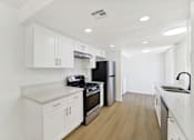 Thumbnail 24 of 31 - Galley kitchen with white cabinetry and gas range at Coventry Square Apartments, Upland, CA 97186