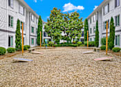 Thumbnail 14 of 28 - A courtyard with a gravel surface and a tree in the middle.