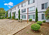 Thumbnail 1 of 28 - A building with grey siding and a gravel area in front.