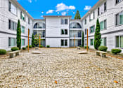Thumbnail 15 of 28 - A courtyard surrounded by apartment buildings with a gravel ground and trees.