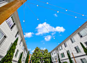 Thumbnail 2 of 28 - Apartment complex with trees and string lights.