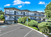 Thumbnail 6 of 21 - A sunny day at a parking lot in front of a multi-story apartment building.