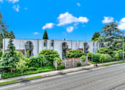 Thumbnail 22 of 28 - A white building with a green tree on top and a fence in front.