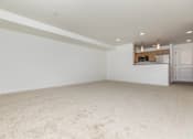 Thumbnail 44 of 52 - A large empty room with a carpeted floor and a kitchen area in the background.
