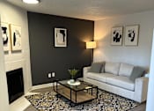 Thumbnail 10 of 25 - A living room with a grey couch, a coffee table, and a fireplace.