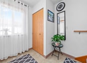Thumbnail 6 of 16 - A room with a wooden door, a small table with a plant, and a mirror on the wall.
