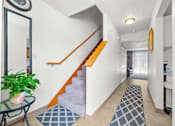 Thumbnail 7 of 16 - A hallway with a staircase and a plant on a table.