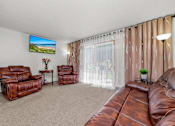 Thumbnail 12 of 16 - A living room with a brown leather couch and a flat screen TV mounted on the wall.