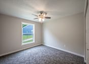 Thumbnail 4 of 8 - A room with a ceiling fan and a window overlooking a blue fence.