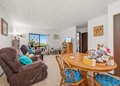 Thumbnail 6 of 11 - A living room with a brown recliner and a wooden table.