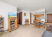 Thumbnail 5 of 11 - A living room with a television, a bookshelf, and a dining area.