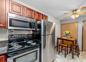 Thumbnail 8 of 16 - A kitchen with a stove, microwave, refrigerator, and a table with chairs.