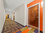 Thumbnail 12 of 18 - A hallway with a wooden door and a carpet with different colored squares.