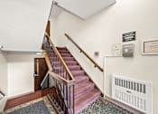 Thumbnail 14 of 18 - A staircase with a red carpet and a white wall with a framed certificate.