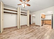 Thumbnail 4 of 18 - A room with a ceiling fan and a kitchen area in the background.
