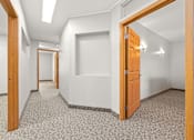 Thumbnail 7 of 23 - A hallway with a carpeted floor and white walls.