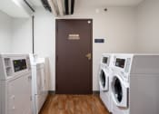 Thumbnail 21 of 22 - a laundry room with two washers and two dryers and a brown door