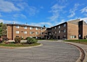 Thumbnail 1 of 7 - A large brick building with a parking lot in front.