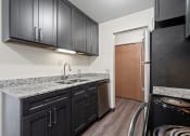 Thumbnail 13 of 20 - a kitchen with black cabinets and granite counter tops and a refrigerator