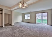 Thumbnail 6 of 7 - A large, empty room with a carpeted floor and a chandelier hanging from the ceiling.
