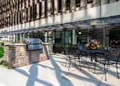 Thumbnail 21 of 34 - a patio with a table and chairs and a grill outside of a building