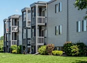 Thumbnail 11 of 15 - A grey apartment building with balconies and bushes in front.