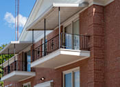 Thumbnail 8 of 10 - A red brick building with a balcony and a white awning.