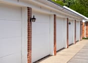 Thumbnail 9 of 10 - A row of white garage doors with brick pillars.