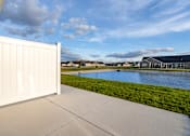 Thumbnail 20 of 23 - A white fence is in the foreground of a bright day with a house and a pond in the background.
