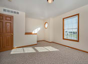 Thumbnail 14 of 14 - A room with a brown door, a window with blinds, and a round mirror on the wall.