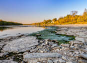 Thumbnail 16 of 16 - A rocky shoreline with a body of water and trees in the background.