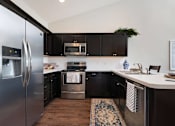 Thumbnail 7 of 23 - A modern kitchen with a stainless steel refrigerator and black cabinets.