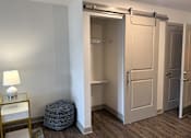 Thumbnail 7 of 19 - A room with a white door, a lamp on a table, and a round ottoman.