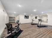 Thumbnail 47 of 62 - a gym with two exercise machines and a tv on the wall at 41 North Apartments, Fort Wayne, IN