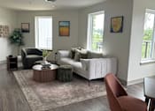 Thumbnail 14 of 19 - A living room with a white couch, a green chair, and a brown ottoman.