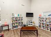 Thumbnail 19 of 40 - A living room with a brown table and a bookshelf filled with books.