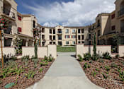 Thumbnail 4 of 50 - A concrete walkway leads through a landscaped courtyard between two rows of apartment buildings.