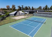 Thumbnail 26 of 35 - A tennis court with a green and blue surface surrounded by a fence.