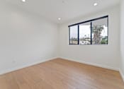 Thumbnail 97 of 119 - Empty room with wooden floor and a window showing a view of trees and a building.
