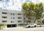 Thumbnail 25 of 28 - a white apartment building with cars parked in front of it