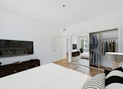 Thumbnail 7 of 16 - A bedroom with a large bed and a wardrobe with clothes hanging.